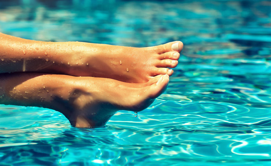 a set of feet dangling over a body of pool water, which have had baby foot peel applied