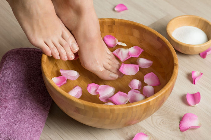 Closeup shot of a woman feet dipped in water with petals in a wooden bowl. Beautiful female feet at spa salon on pedicure procedure. Shallow depth of field with focus on feet. Baby foot Peel