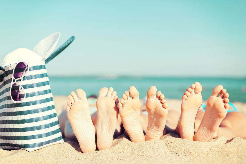 3 sets of feet lie on the beach, the ocean in the background