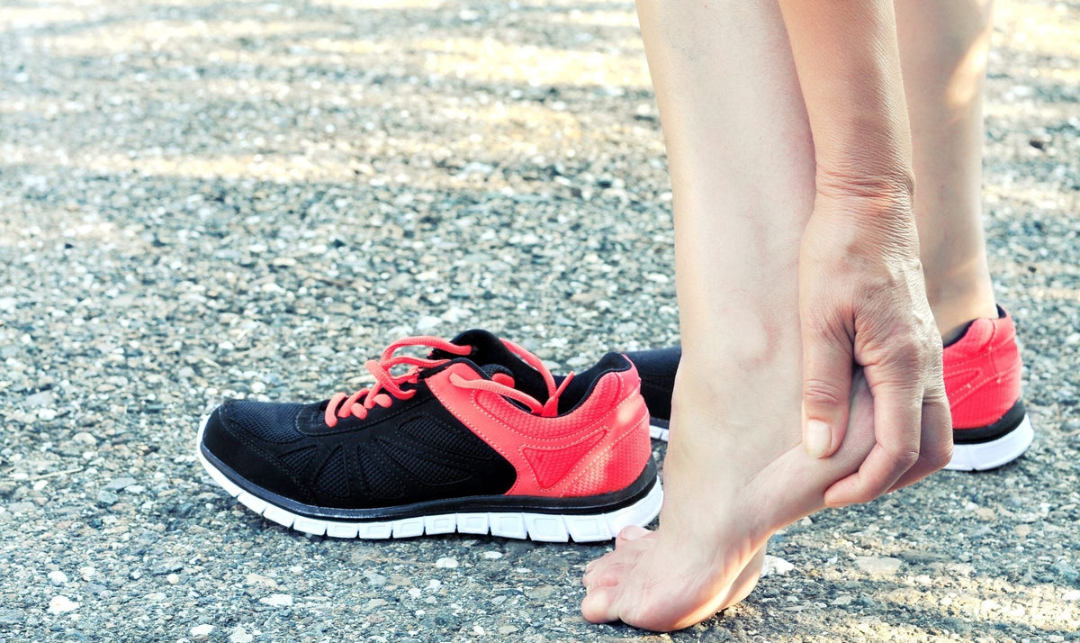 A person stretches their feet near a pair of running shoes