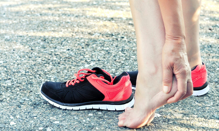 A person stretches their feet near a pair of running shoes