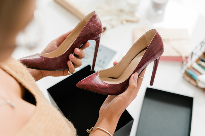 Pair of fashionable leather high-heeled shoes held by young female shopper