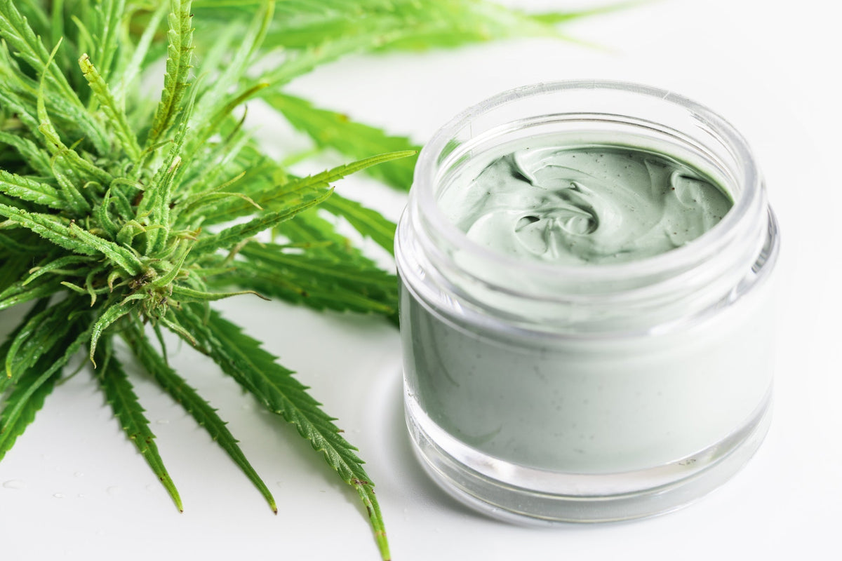 A jar of CBD foot cream sits near some greenery