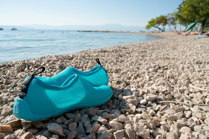 Pair of aqua blue water shoes on a beach next to the water