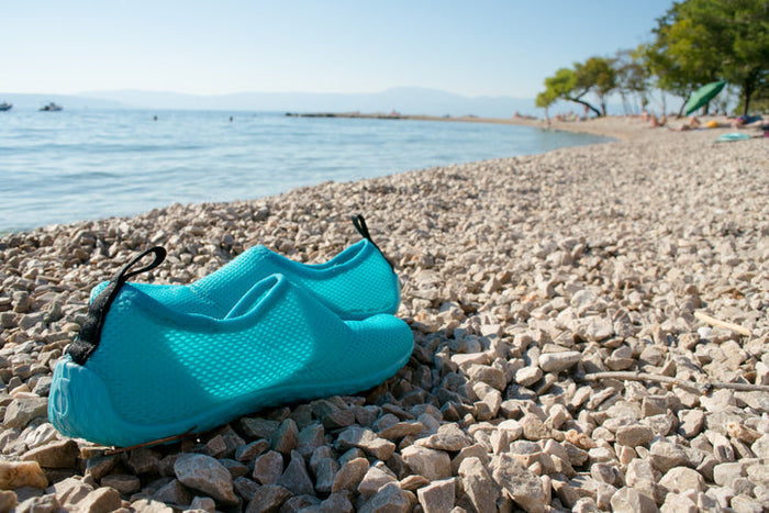 Pair of aqua blue water shoes on a beach next to the water
