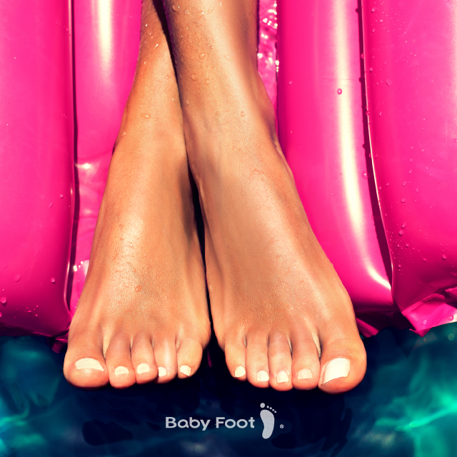a pair of feet - crossed - dangling off of the end of a pink, inflatable pool float matress, above the surface of the water, with the Baby Foot logo at the bottom